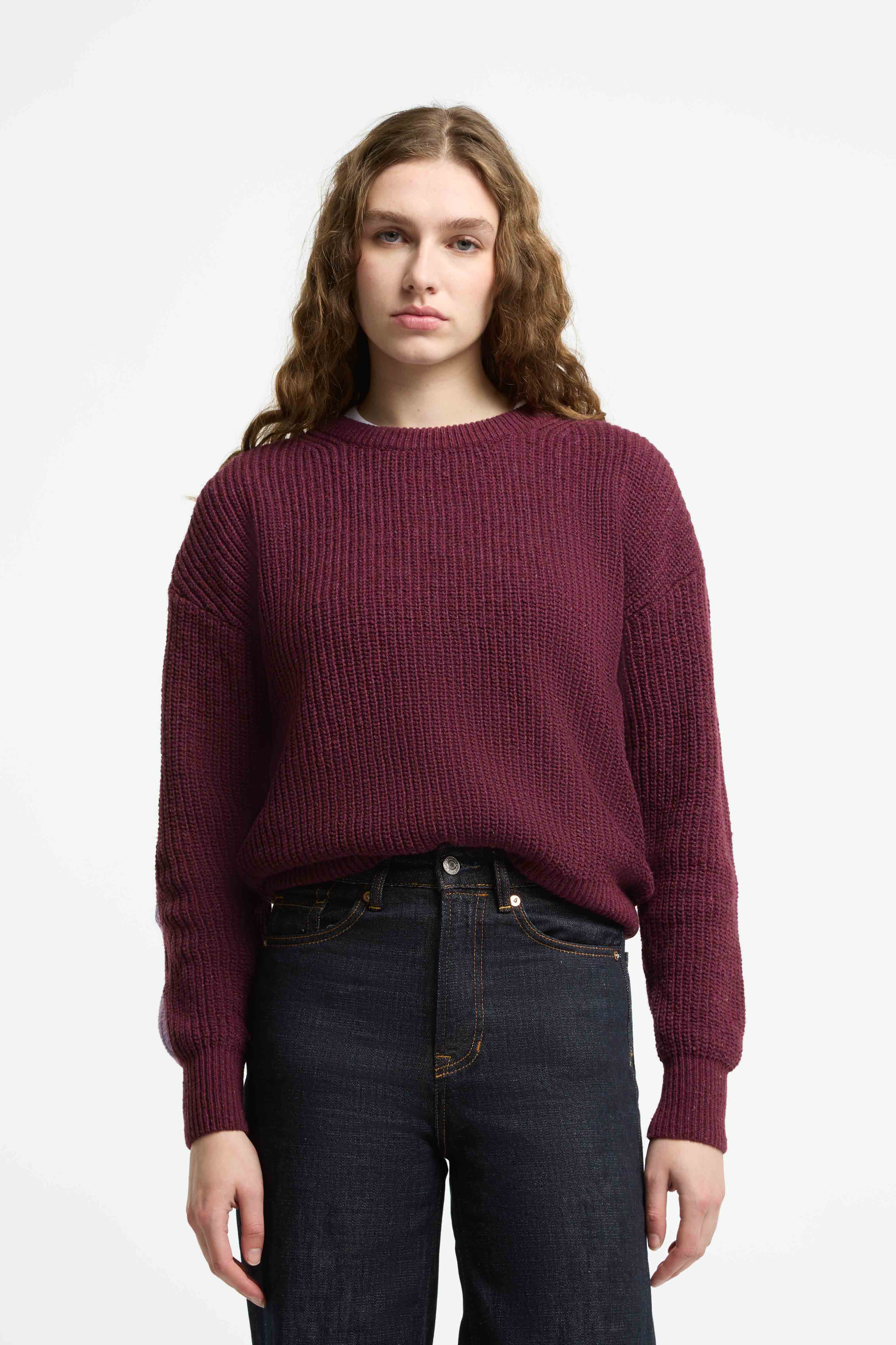 Woman wearing a burgundy sweater and dark jeans on a white background