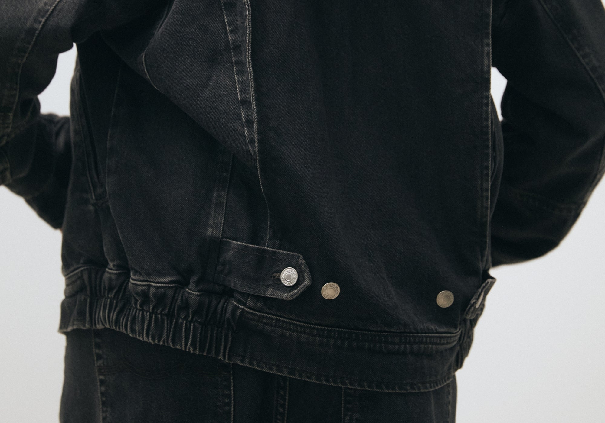 Close-up of a black denim jacket with visible buttons on a light gray background